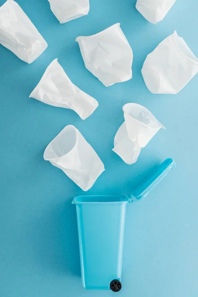 Vista superior de copos de plástico branco caindo lata de lixo de brinquedo no fundo azul — Fotografia de Stock
