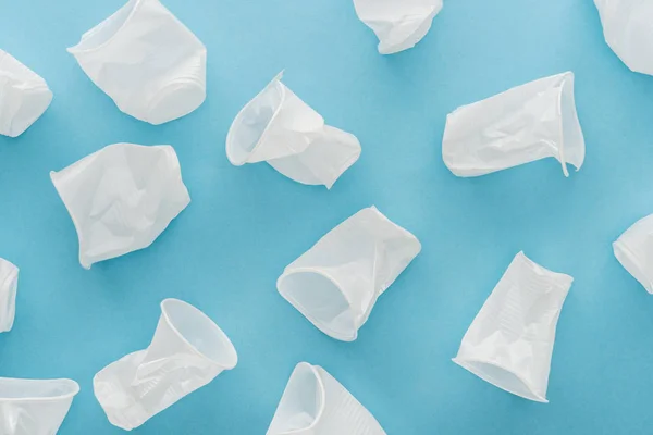 Vue de dessus des tasses blanches, froissées et en plastique sur fond bleu — Photo de stock