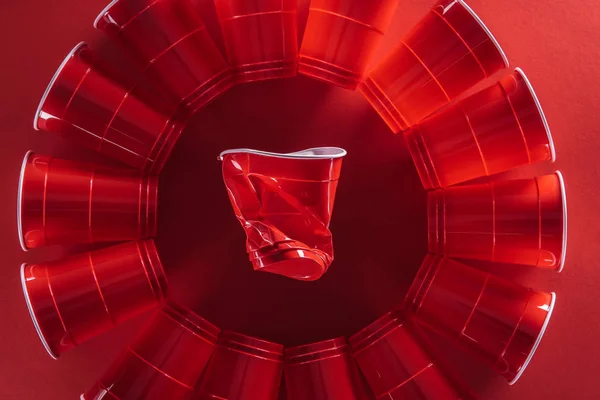 Flache Lage mit hellen und bunten Plastikbechern auf rotem Hintergrund — Stockfoto