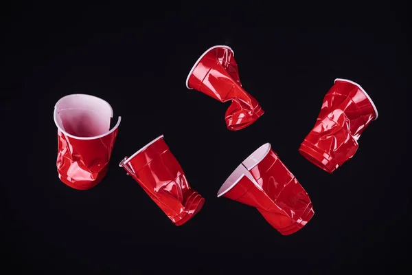 Vista superior de brilhante e colorido, copos de plástico vermelho isolado em preto com espaço de cópia — Fotografia de Stock