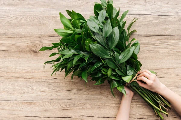 Vue recadrée du fleuriste tenant un bouquet vert sur une surface en bois — Photo de stock