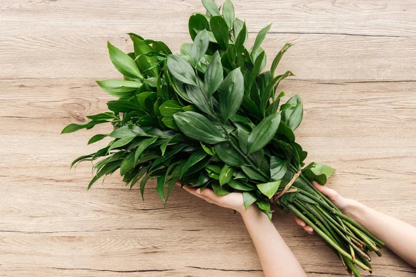 Cropped view of florist holding green bouquet on wooden surface — Stock Photo