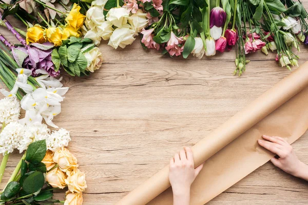 Vista cortada de florista com papel kraft e flores coloridas na superfície de madeira — Fotografia de Stock