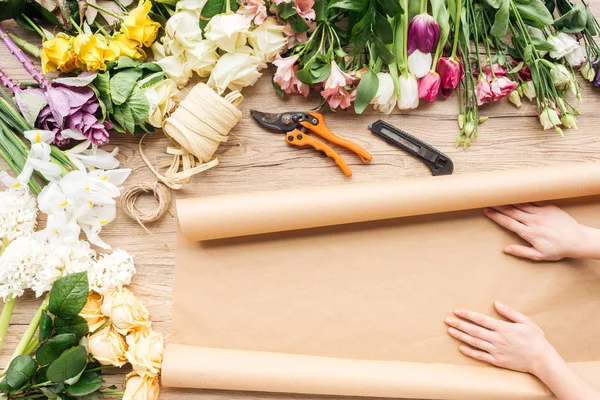 Vue recadrée du fleuriste avec du papier artisanal et des fleurs colorées sur une surface en bois — Photo de stock