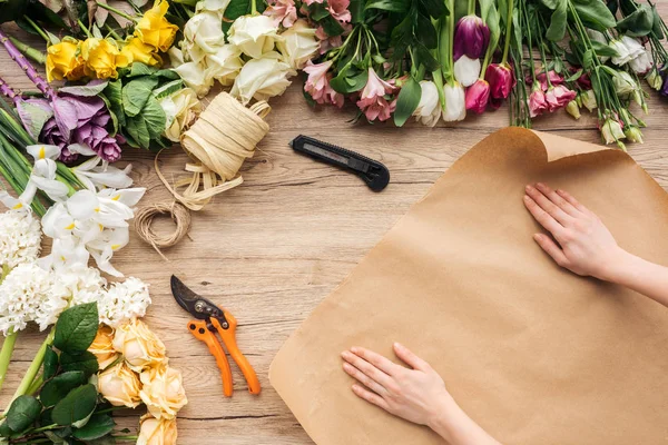 Vue recadrée du fleuriste avec du papier artisanal et des fleurs colorées sur une surface en bois — Photo de stock