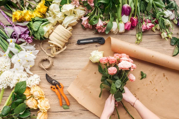 Partial view of florist making flower bouquet on wooden surface — Stock Photo