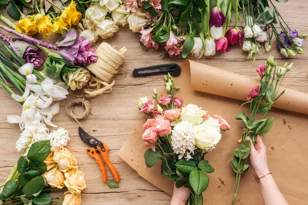 Vista parziale di fiorista che fa mazzo di fiori su superficie di legno — Foto stock