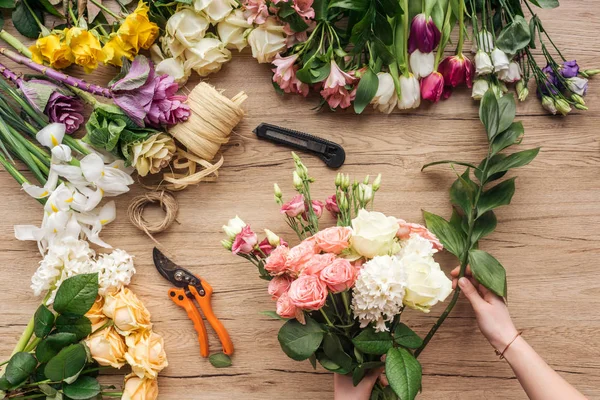 Partial view of florist making flower bouquet on wooden surface — Stock Photo