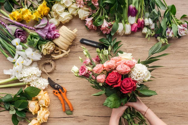 Vista cortada de florista segurando buquê de flores frescas na superfície de madeira — Fotografia de Stock