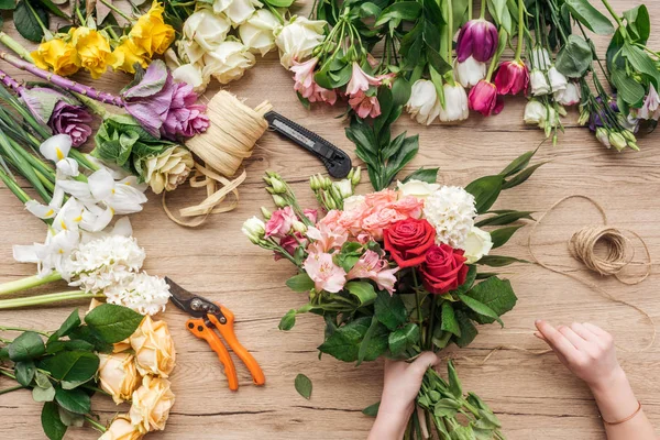 Cropped view of florist holding bouquet of fresh flowers on wooden surface — Stock Photo