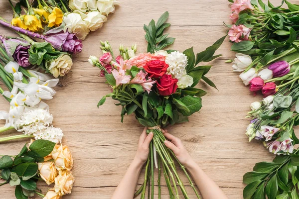 Vista cortada do florista segurando buquê de flores na mesa de madeira — Fotografia de Stock