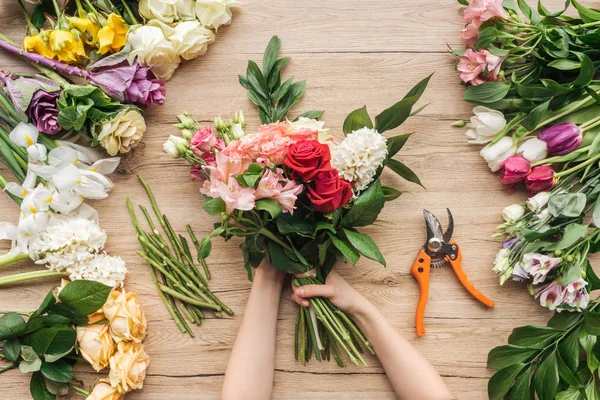Cropped view of florist holding flower bouquet on wooden table — Stock Photo