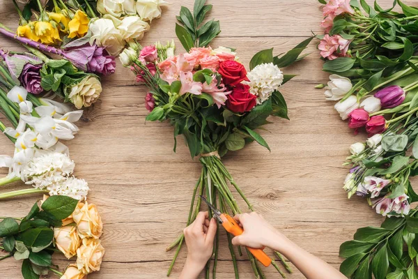 Teilansicht Blumenhändler schneidet Blütenstiele auf Holzoberfläche — Stockfoto