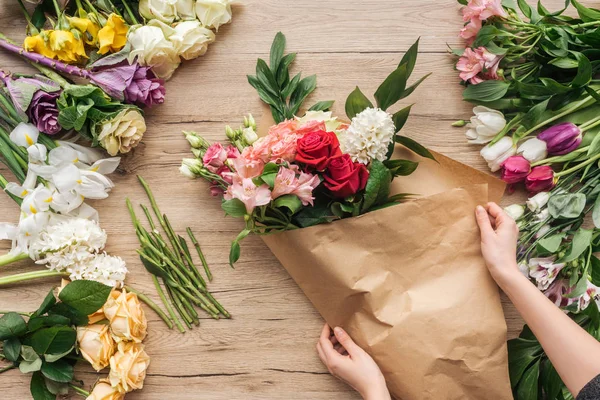 Vista ritagliata del fiorista che fa mazzo di fiori sulla superficie di legno — Foto stock