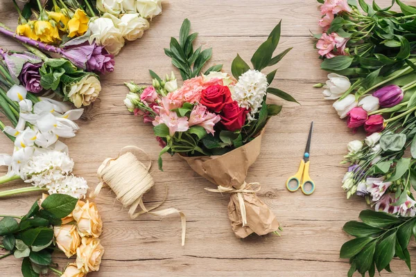 Вид на букет цветов в бумажной обертке и ножницы на деревянной поверхности — стоковое фото