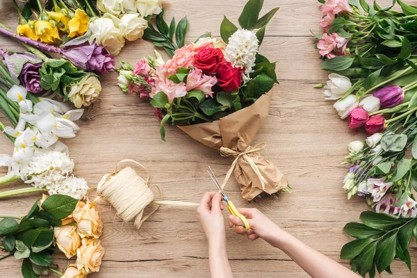 Vista ritagliata del fiorista che fa mazzo di fiori sulla superficie di legno — Foto stock