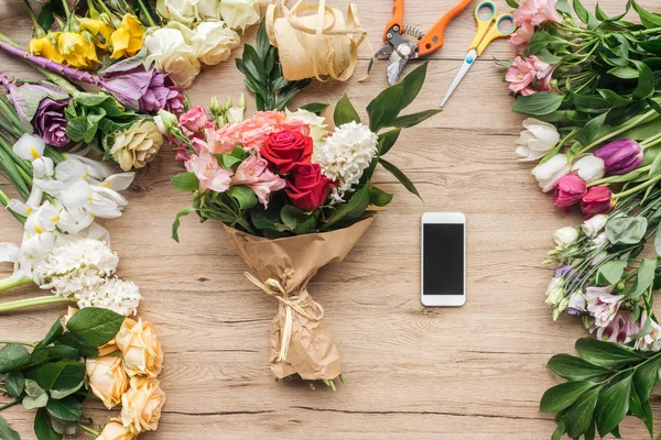 Fiori freschi e smartphone con schermo bianco su superficie in legno — Foto stock