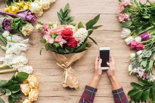 Vista parcial de la floristería con teléfono inteligente con pantalla en blanco cerca de flores en superficie de madera - foto de stock