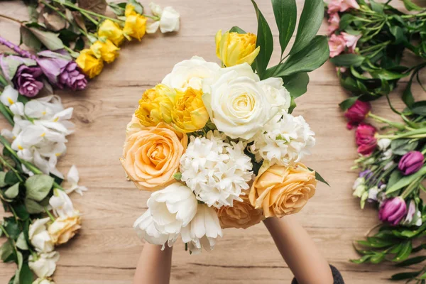 Partial view of florist holding bouquet of fresh flowers on wooden surface — Stock Photo
