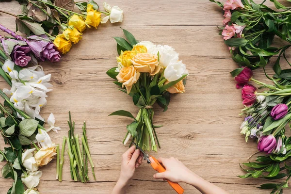Vue recadrée du fleuriste coupant des tiges de fleurs en bouquet sur une surface en bois — Photo de stock