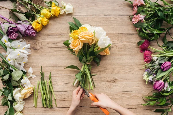 Vista cortada de florista talos de flores de corte em buquê na superfície de madeira — Fotografia de Stock