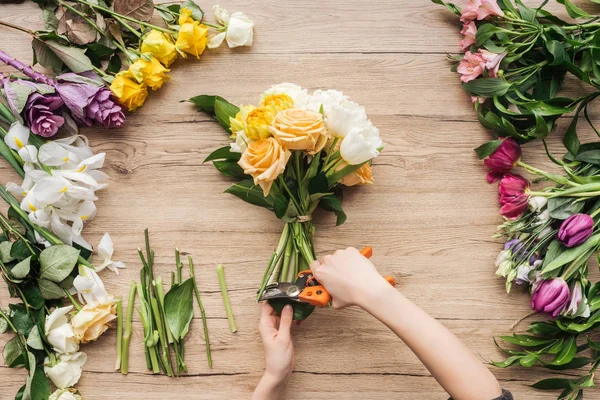 Vue recadrée du fleuriste coupant des tiges de fleurs en bouquet sur une surface en bois — Photo de stock