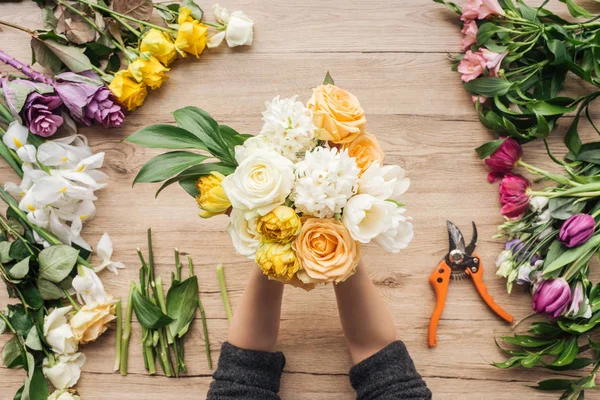 Teilansicht des Blumenhändlers, der einen Strauß frischer Blumen auf einer Holzoberfläche hält — Stockfoto