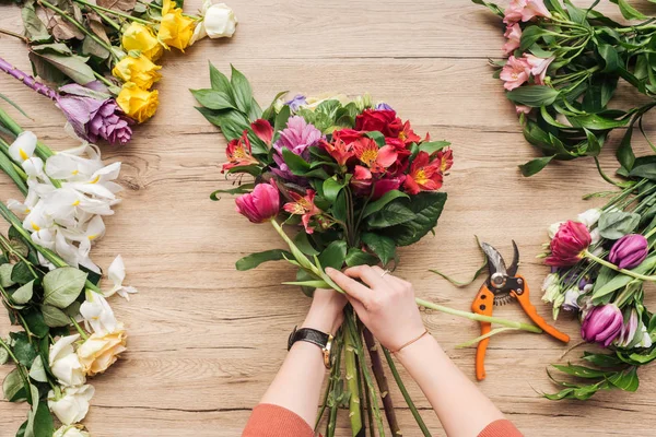 Vista ritagliata del fiorista che fa mazzo di fiori sulla superficie di legno — Foto stock