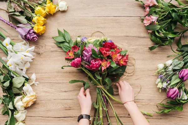 Vista ritagliata del fiorista che fa mazzo di fiori sulla superficie di legno — Foto stock