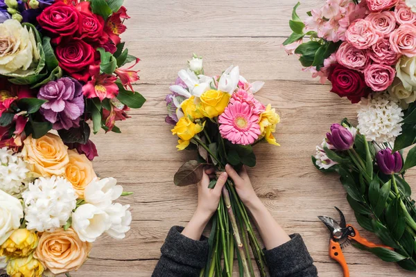 Vista cortada de florista fazendo buquê de flores na superfície de madeira — Fotografia de Stock