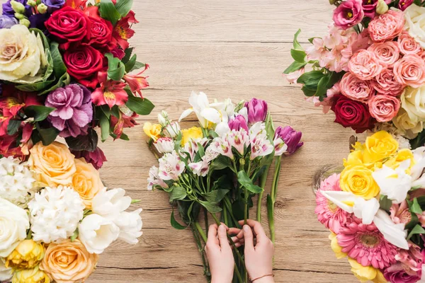 Vista ritagliata del fiorista che fa mazzo di fiori sulla superficie di legno — Foto stock