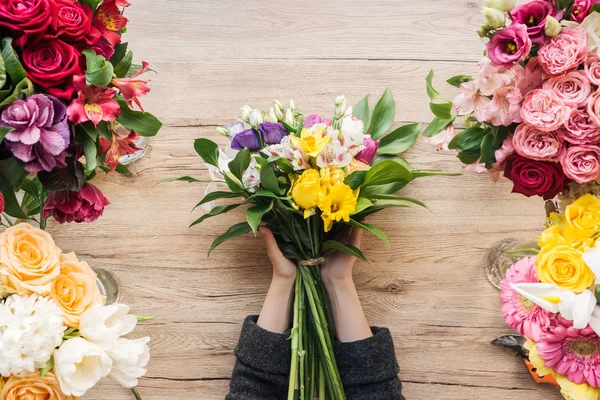 Partial view of florist holding bouquet of fresh flowers on wooden surface — Stock Photo