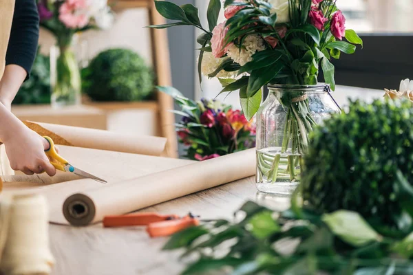 Partial view of florist cutting craft paper on table with flowers and plants — Stock Photo