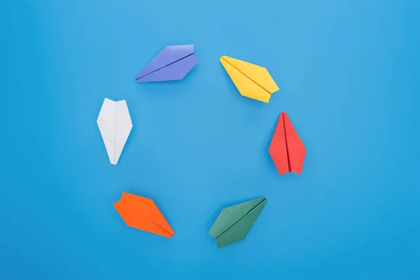 Flat lay with colorful paper planes on blue surface — Stock Photo