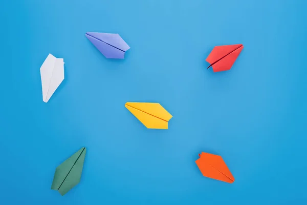 Flat lay with colorful paper planes on blue surface — Stock Photo