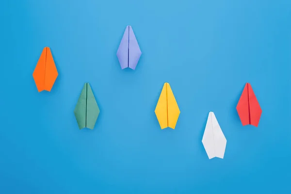 Flat lay with colorful paper planes on blue surface — Stock Photo