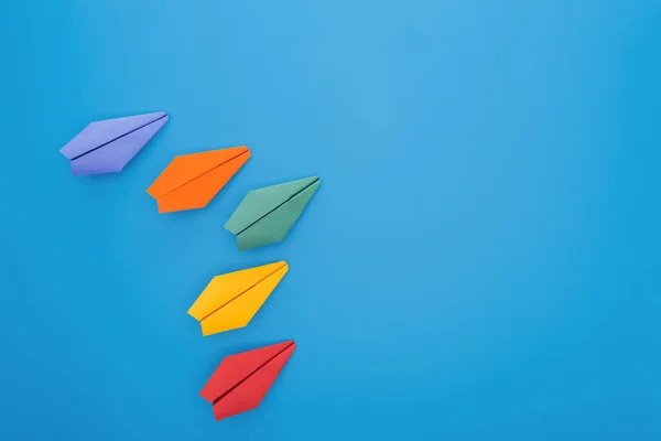 Flat lay with colorful paper planes on blue surface — Stock Photo