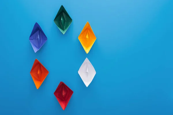 Flat lay with colorful paper boats on blue surface — Stock Photo