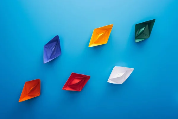 Colocación plana con barcos de papel de colores en la superficie azul - foto de stock