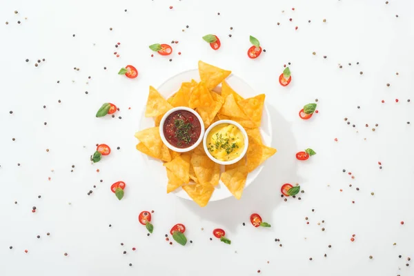 Blick von oben auf leckere Nachos und Soßen auf Teller, Gewürze und in Scheiben geschnittene Chilischoten mit Basilikumblättern — Stockfoto