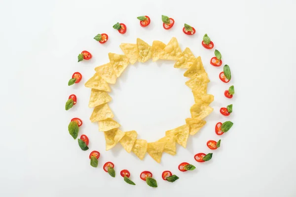 Top view of sliced chili peppers and tasty nachos with basil leaves on white background — Stock Photo