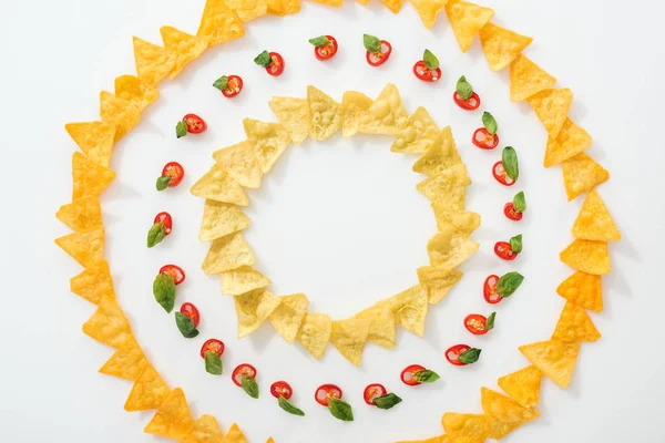 Vue de dessus des piments tranchés et des nachos savoureux avec des feuilles de basilic sur fond blanc — Photo de stock