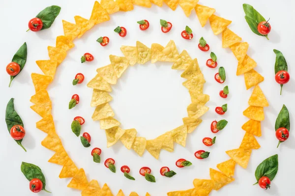 Vista superior de chiles en rodajas y sabrosos nachos con hojas de albahaca y tomates cherry - foto de stock