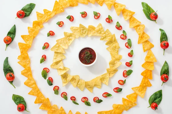 Вид сверху на нарезанный перец чили, соус и вкусные начос с листьями базилика и помидорами черри — стоковое фото