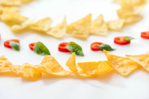 Foco seletivo de nachos saborosos e pimentas com manjericão sobre fundo branco — Fotografia de Stock