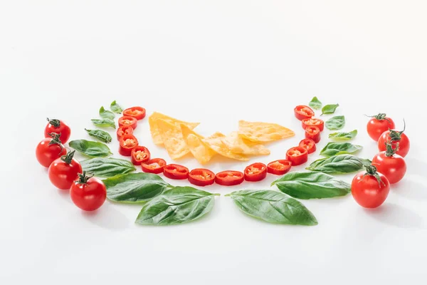Flat lay with nachos, cut chili peppers, basil leaves and ripe cherry tomatoes on white background — Stock Photo