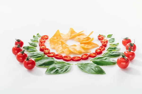 Acostado plano con nachos, chiles cortados, hojas de albahaca y tomates cherry maduros - foto de stock
