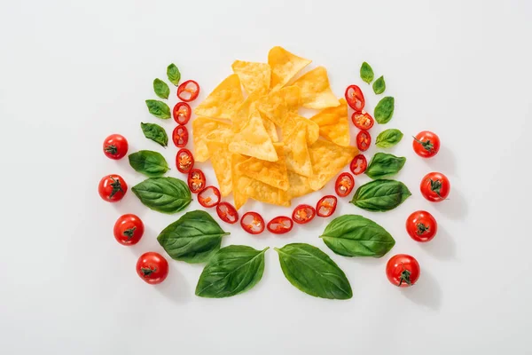 Acostado plano con nachos, chiles cortados, hojas de albahaca y tomates cherry maduros - foto de stock