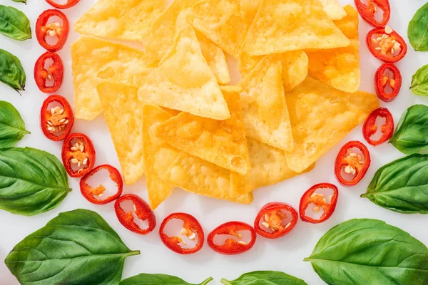 Vista dall'alto di nachos, peperoncino tagliato e foglie di basilico su sfondo bianco — Foto stock