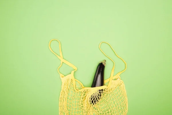 Top view of ripe eggplant in yellow string bag on light green background — Stock Photo